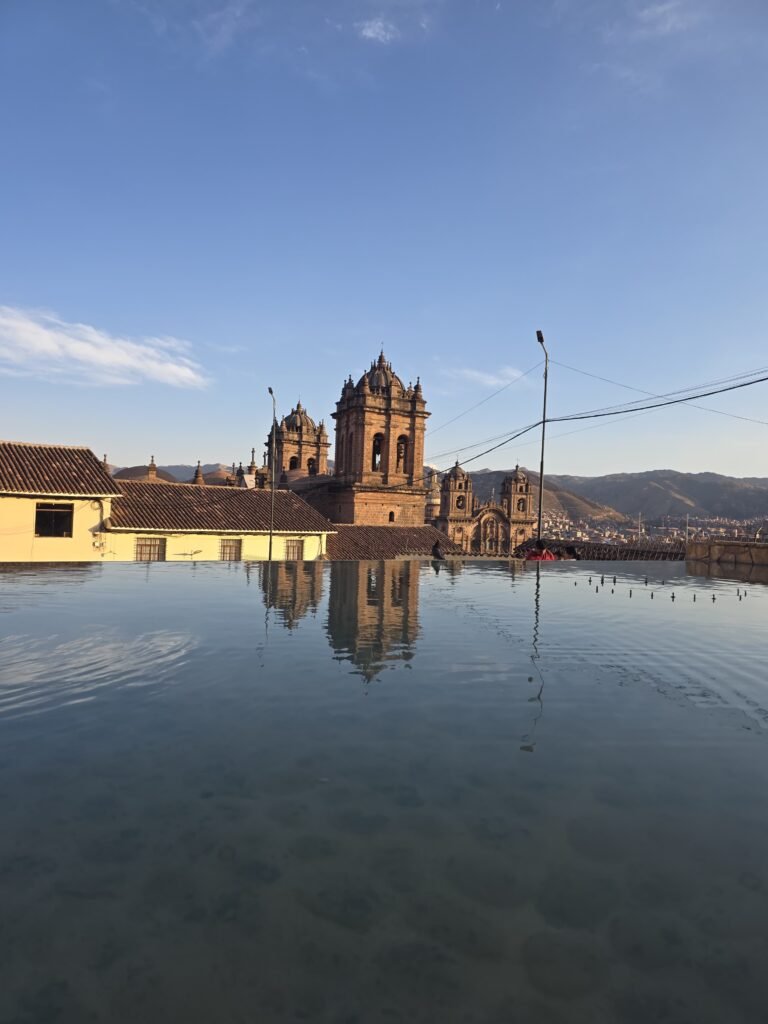 Catedral de Cusco reflejada en el agua de la plaza, con arquitectura colonial y montañas andinas al fondo, Perú.